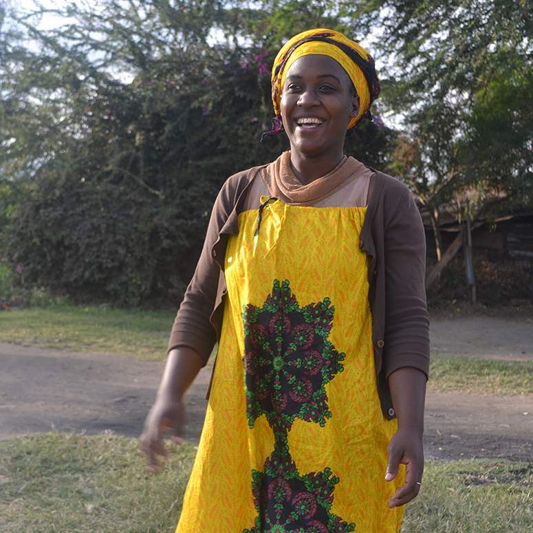 Gladness - En Tanzaniansk kvinne smiler i gul kjole med afrikansk mønster